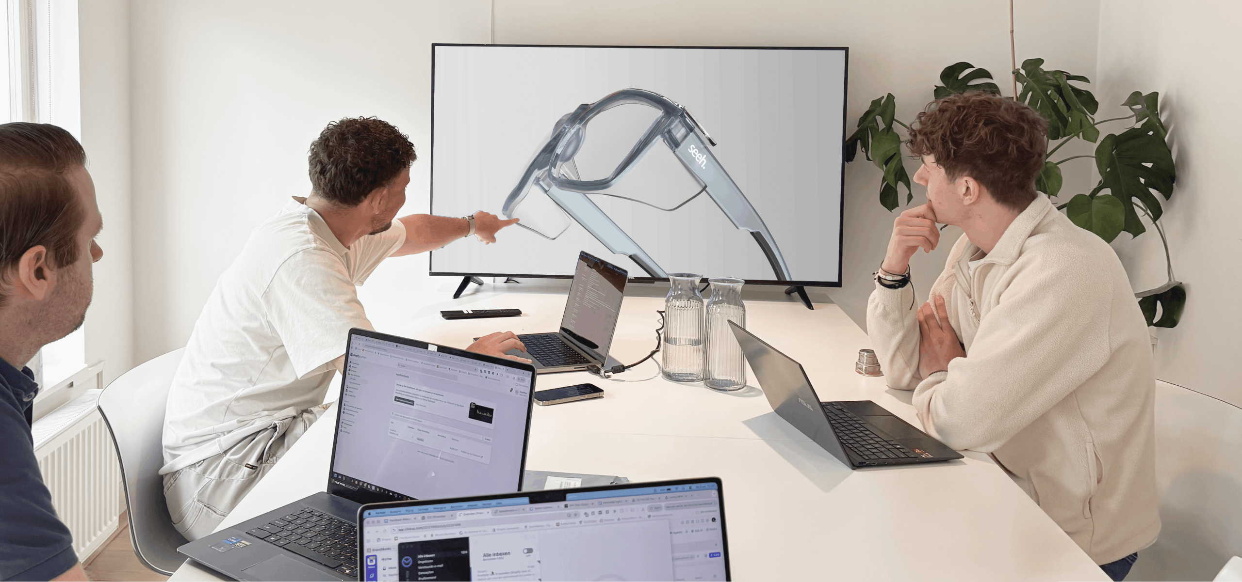 Drie collega's bekijken een 3D-model van een Seeh veiligheidsbril op een groot scherm tijdens een overleg